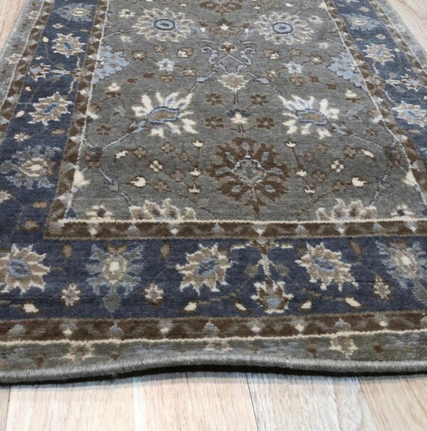 Charcoal gray medium pile rug with traditional blue, brown, and cream floral designs on light wood flooring.