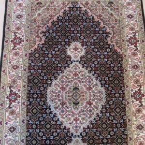 Low-pile traditional rug featuring a dark field, light ivory borders, and a prominent central arch design on wood floor.