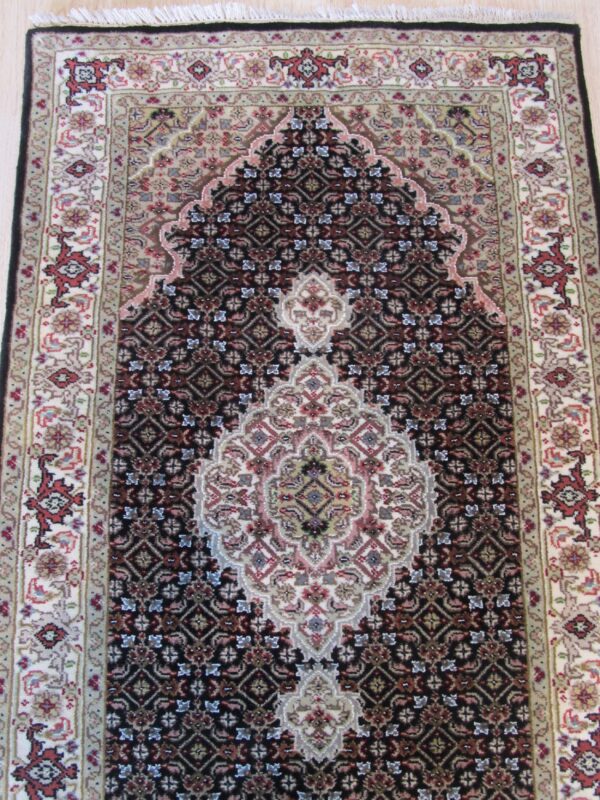 Low-pile traditional rug featuring a dark field, light ivory borders, and a prominent central arch design on wood floor.