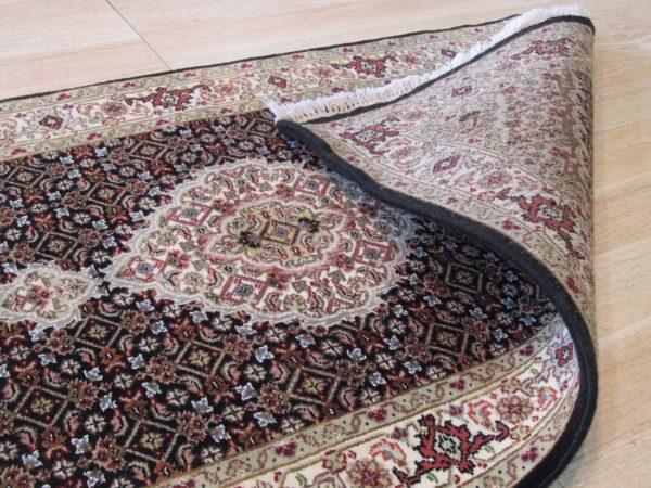 Traditional black, cream, and red medallion rug partially curled on light wood plank flooring.