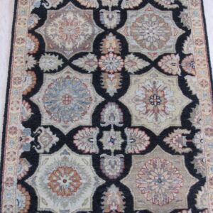 Low-pile rug with a black, beige, and rust geometric floral pattern resting on light hardwood.