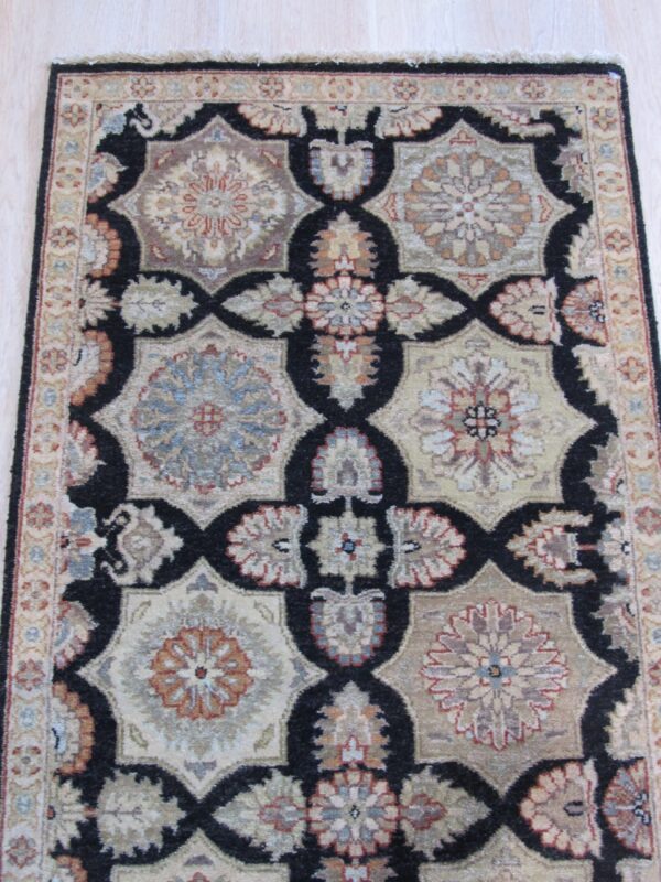 Low-pile rug with a black, beige, and rust geometric floral pattern resting on light hardwood.