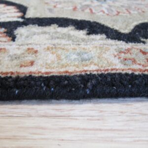 A detailed shot shows the thick black edging and patterned tan border of a rug on light wood floor.