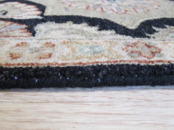 A detailed shot shows the thick black edging and patterned tan border of a rug on light wood floor.