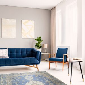 A traditional blue rug with beige geometric medallions lies beneath a modern blue sofa and armchair.