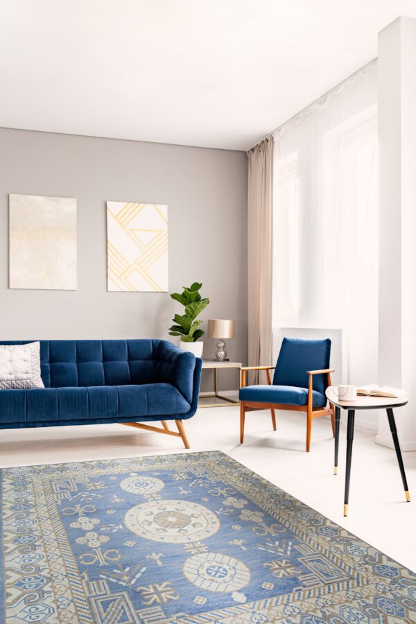 A traditional blue rug with beige geometric medallions lies beneath a modern blue sofa and armchair.