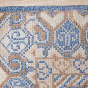 Geometric blue, tan, and cream high-pile rug with fringed edge resting on light wood floor.