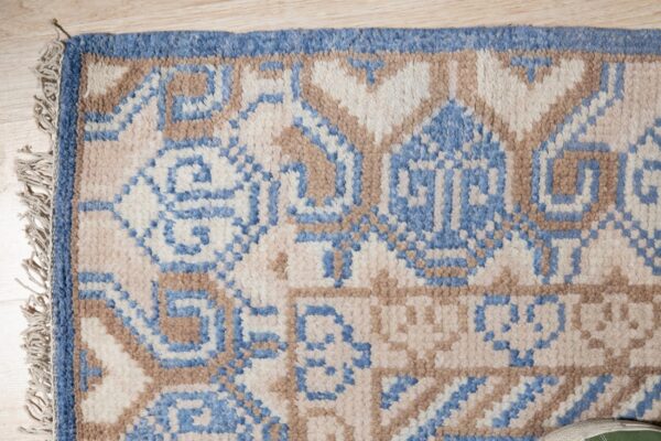 Geometric blue, tan, and cream high-pile rug with fringed edge resting on light wood floor.