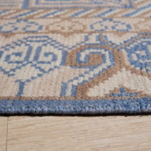 Close-up of a blue, beige, and brown geometric rug edge resting on light wood flooring.