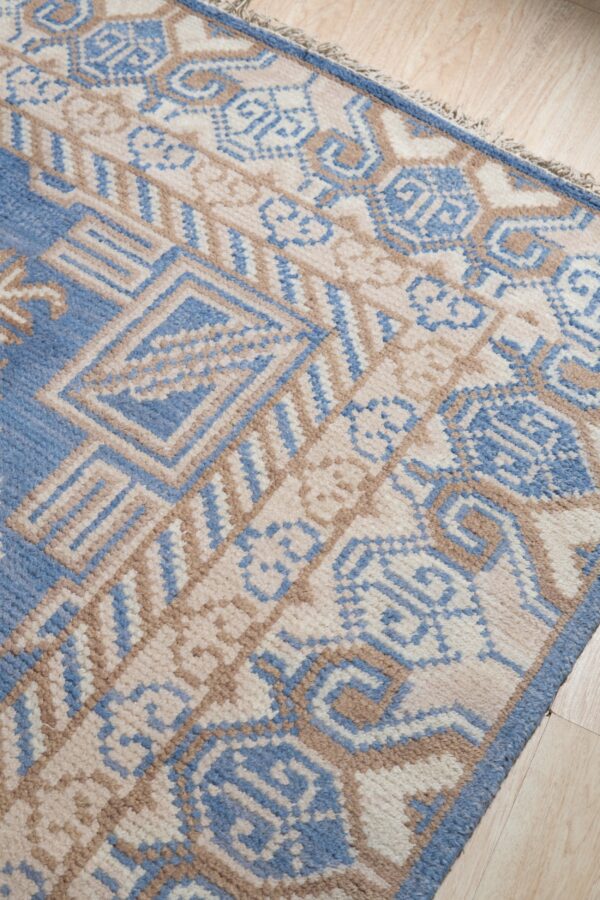 Textured pile rug with blue, beige, and brown geometric tribal patterns on light wood flooring.