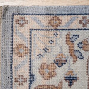 Chunky woven rug with blue-gray, cream, and brown traditional patterns and fringe on wood floor.