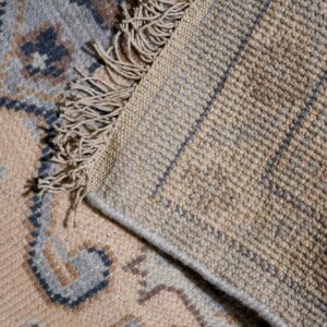Beige rug pile with blue and brown patterns folds over showing a textured tan backing and fringe.