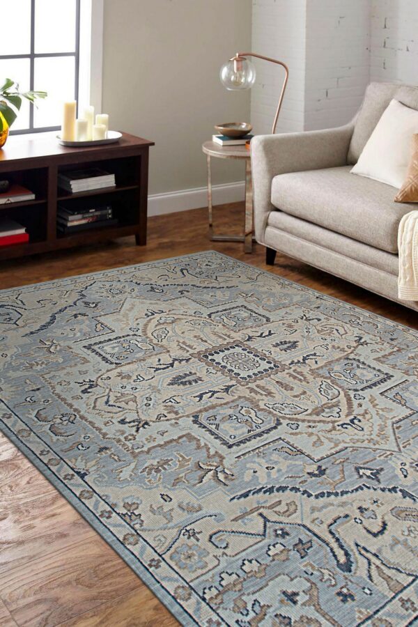 Geometric blue and brown traditional area rug on wood flooring next to a tan upholstered sofa.