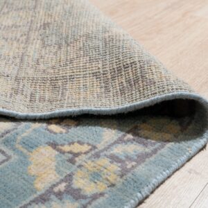 Detail of a blue and beige patterned rug curled over, showing its backing texture on light wood flooring.
