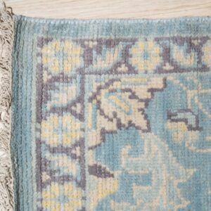 Chunky pile rug in blue, gray, and pale yellow with fringe visible against light wood flooring.