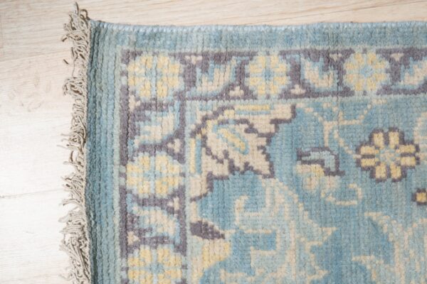 Chunky pile rug in blue, gray, and pale yellow with fringe visible against light wood flooring.