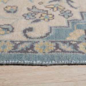 The edge of a beige rug with blue, yellow, and gray traditional patterns lies on wood flooring.