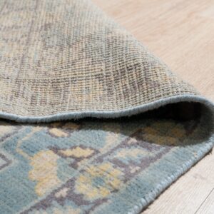 Muted blue and tan patterned rug folded to show its tight woven backing on light wood floor.