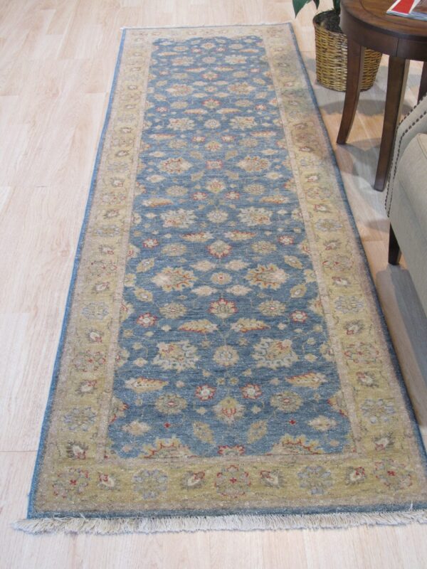 Traditional runner rug featuring a blue field and gold floral border rests on light wood flooring.