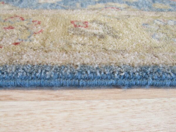 Thick pile rug with tan, blue, and red floral pattern rests on a blonde wood floor.