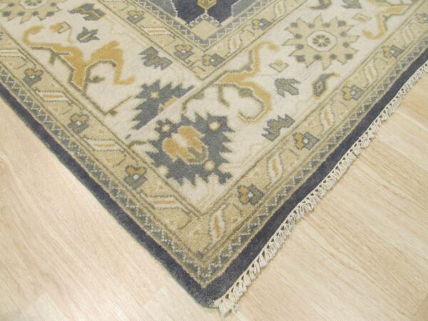 Close-up of a traditional patterned rug corner in cream, gold, and slate blue on light wood flooring.