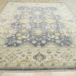 Traditional blue-gray rug with ivory and yellow geometric patterns lying on light wood planks.