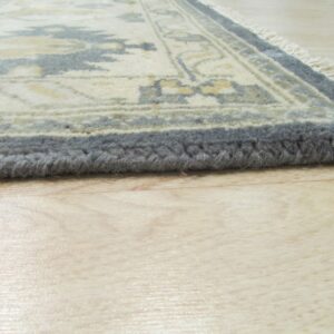 Cream and blue traditional pattern rug with thick pile edges rests on reflective light wood floor.