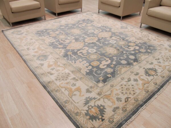 Blue and cream patterned area rug featuring tan accents, centered among four neutral armchairs on light wood flooring.