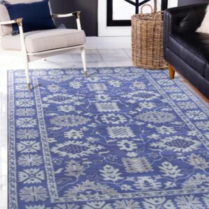 Blue traditional rug with gray floral patterns covering white tiled floor between an armchair and a black sofa.