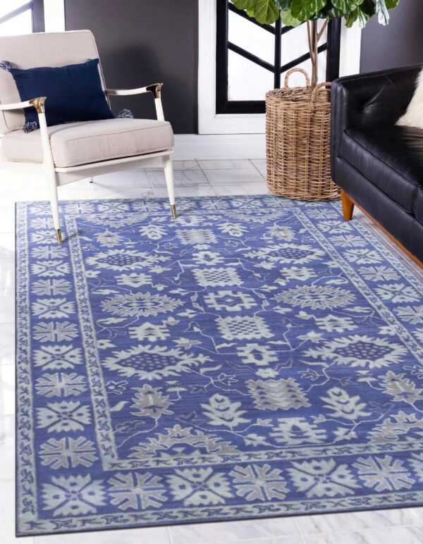 Blue traditional rug with gray floral patterns covering white tiled floor between an armchair and a black sofa.