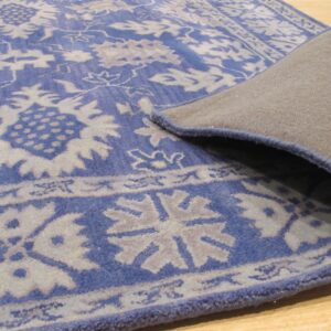 Blue and light gray floral rug displays its tan backing and serged edge on light wood floor.