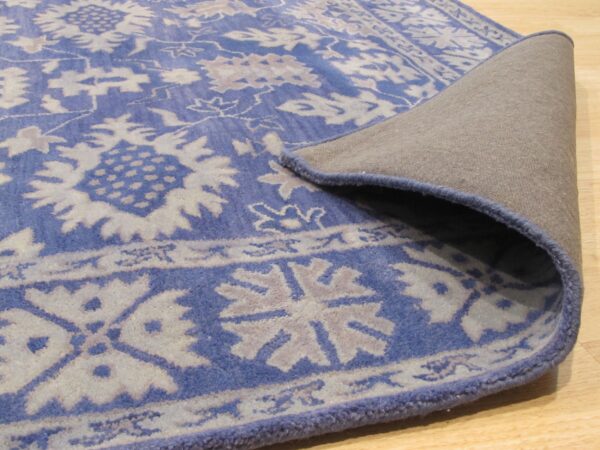 Blue and light gray floral rug displays its tan backing and serged edge on light wood floor.
