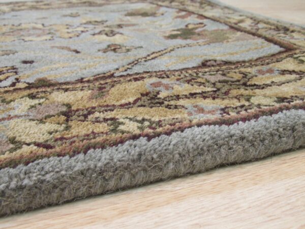 The thick, light gray edge and blue floral pattern of the rug are visible on light wood planks.
