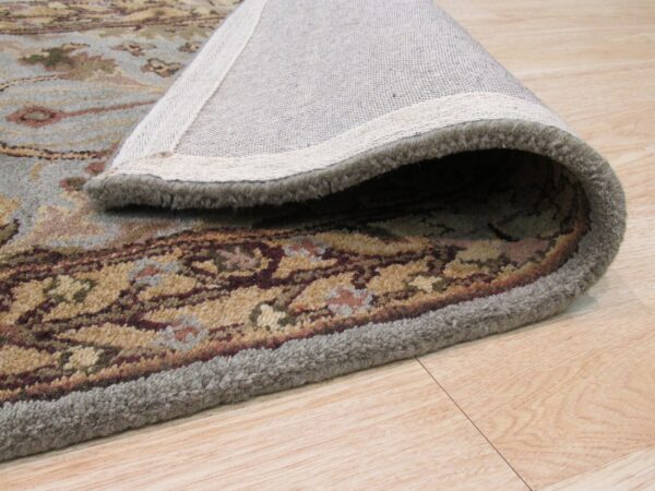 Plush blue and tan patterned rug rolled to reveal its backing on light hardwood flooring.