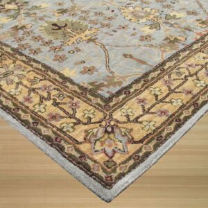 Ornate floral rug corner in slate blue, gold, and green resting on light wood flooring.