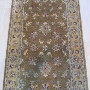 Muted olive runner rug with a repeating floral pattern and a beige border, displayed on pale wood planks.
