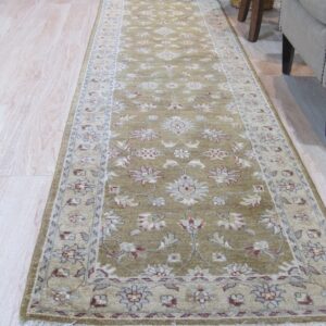 Green runner rug with cream and red traditional floral pattern on light wood floor near upholstered furniture.