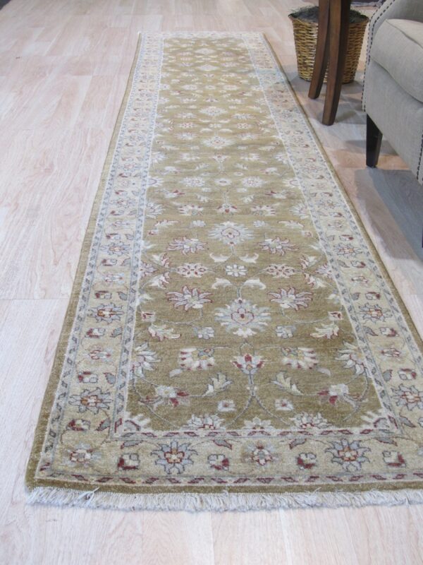 Green runner rug with cream and red traditional floral pattern on light wood floor near upholstered furniture.