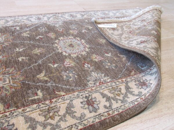 Brown traditional rug with floral motifs and a light border, rolled on light wood plank flooring.