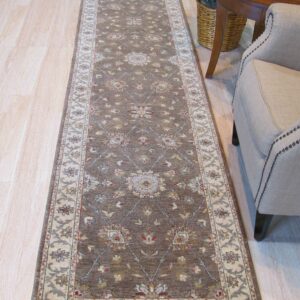 Brown runner rug with floral medallions and cream borders rests on light wood floor next to an armchair.