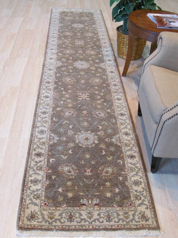 Brown runner rug with floral medallions and cream borders rests on light wood floor next to an armchair.