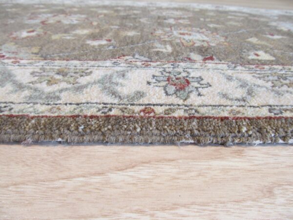 A close-up view of the thick, brown pile edge and floral border pattern on light wood floor.