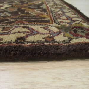 Thick brown rug edge and traditional multi-colored pattern resting on pale blonde wood flooring.