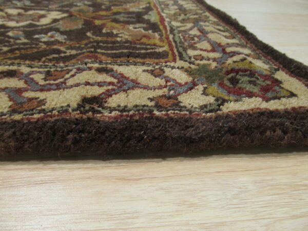 High-pile rug edge in dark brown and multicolored floral pattern rests on light wood flooring.
