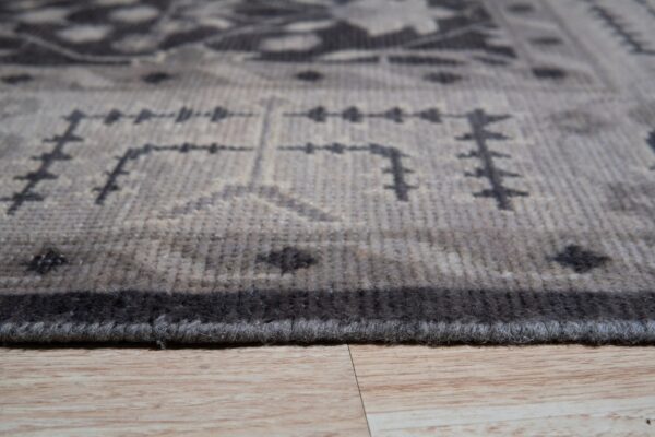 Low-angle view of a short-pile gray and charcoal patterned rug resting on light wood planks.