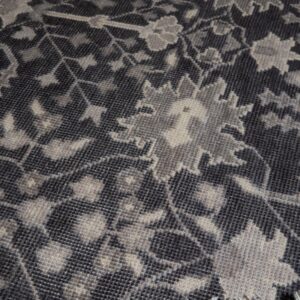 Dark grey rug close-up showing a faded floral pattern and light-colored fringe.