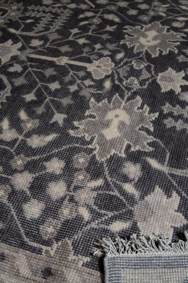 Dark grey rug close-up showing a faded floral pattern and light-colored fringe.