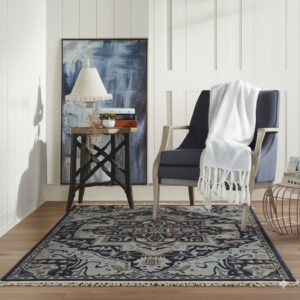 Navy and grey traditional rug with fringe edges lies under a blue armchair and dark side table.