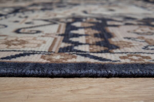 Textured dark blue rug binding and tribal pattern edge resting on light brown wood flooring.