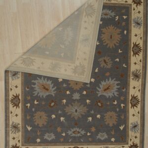 Dark gray floral rug featuring cream, tan, and blue accents, partially folded on light wood planks.